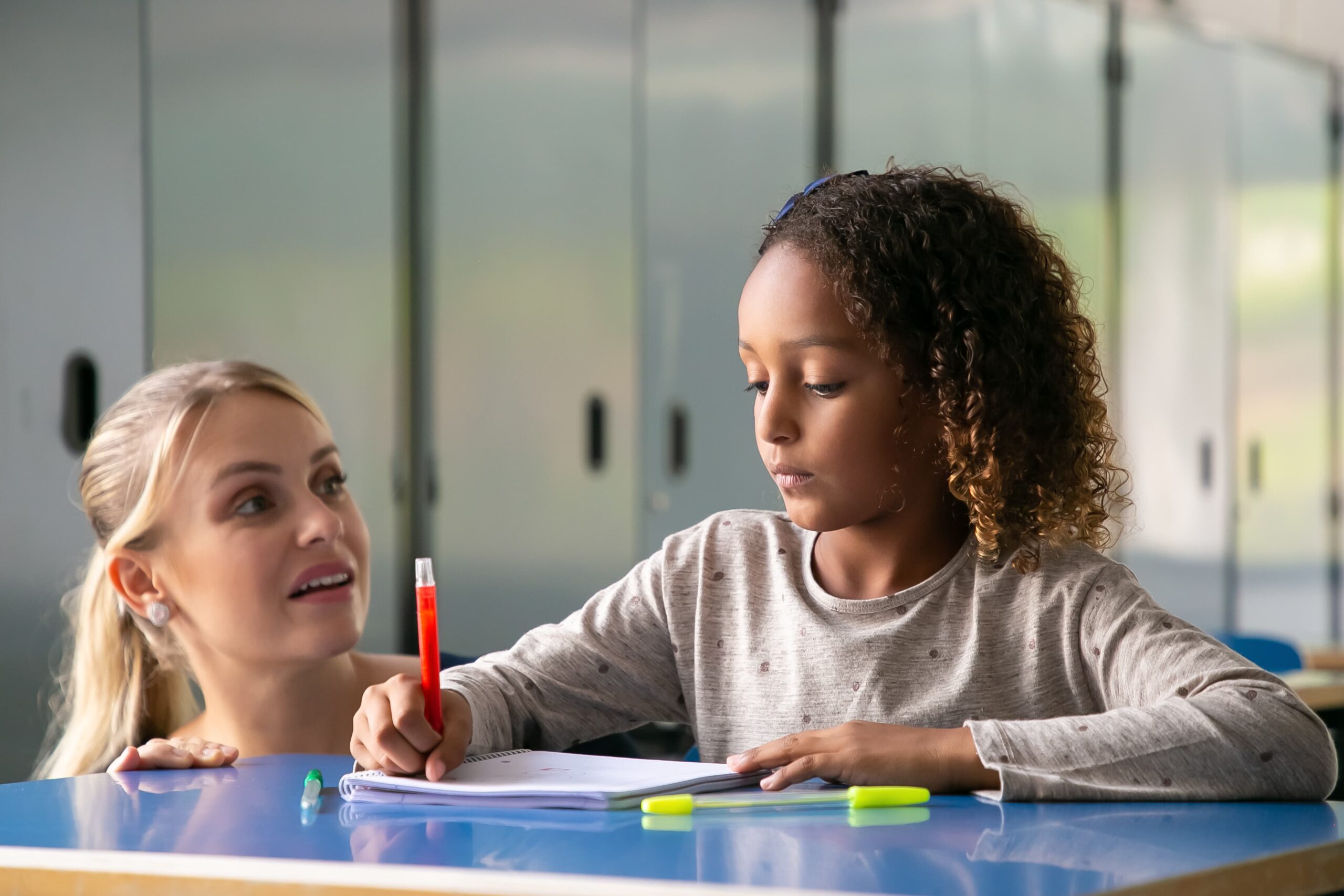 positive female school teacher helping curly haired girl her task 1 scaled