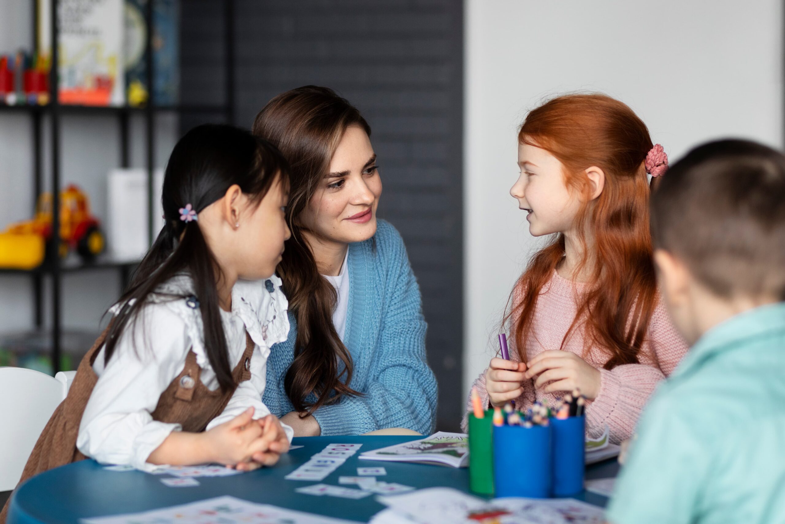 medium shot kids sitting table with teacher 1 scaled