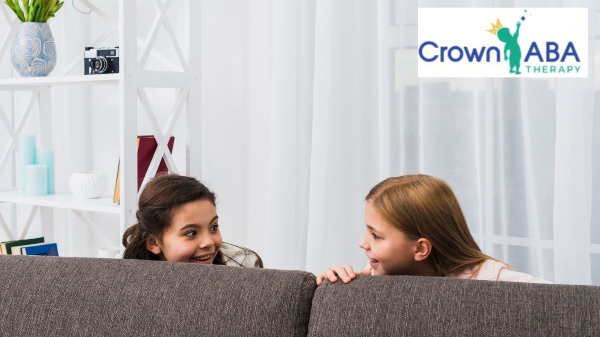 Two children practice ABA communication skills through pretend play in the living room.