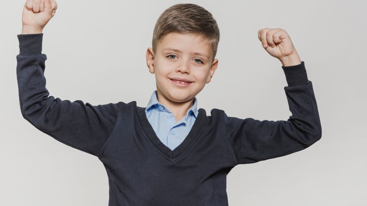 Young boy practices ABA social skills, raising arms confidently during a therapy activity.